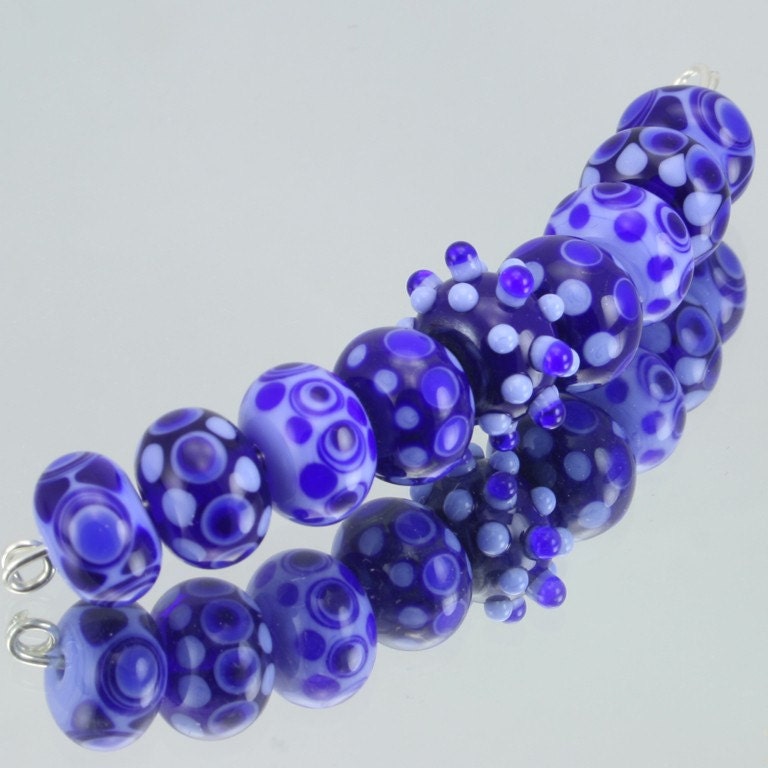 A set of 9 handmade lampwork beads each with layers of dots on top of dots in shades of blue.